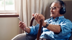   Person sitting in a chair while holding a phone and a cane and wearing headphones