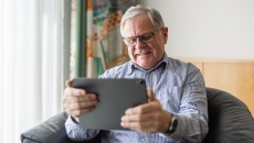 Person sitting in a chair smiling while looking at a tablet