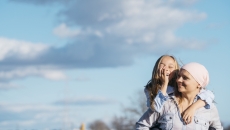 
  Person wearing a scarf on their head holding a child on their back with the sky behind them
