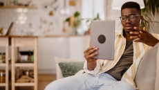 Person sitting on the couch in a home while holding up a tablet in front of them