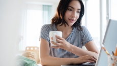 
  Person sitting at a computer holding a coffee cup with a striped shirt on
