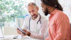 Healthcare provider sitting next to another individual while both are looking at a tablet