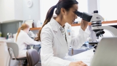 
  Person sitting down looking into a microscope while wearing a lab coat
