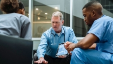 
  Three healthcare providers sitting around a table looking at a tablet
