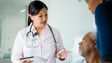 Doctor holding a tablet and standing by a patient and another individual