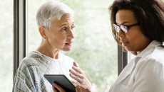 
  Healthcare provider talking to a patient in a hospital gown while both look at a tablet
