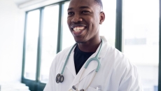 
  Healthcare provider smiling while wearing a lab coat and stethoscope 
