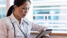 Person sitting by a window wearing a stethoscope and looking at a tablet