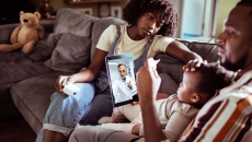 
  Two people sitting on a couch with a child sitting on one's lap while talking to a healthcare provider on a computer 
