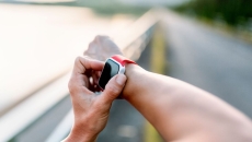 A person wearing a wearable device on their right wrist and touching the device with their left hand