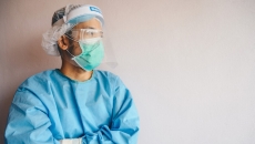 Healthcare worker in PPE stands with their arms crossed looking towards the side