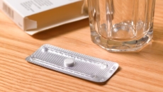 Moring after pill in its packaging on a table next to an empty glass