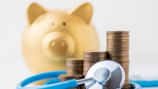 A piggy bank next to a stethoscope and a pile of coins.