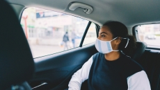 Person in a face mask sits in the back of a car looking out the window