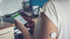 Woman checking glucose level with a remote sensor and mobile phone.