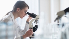 A lab technician analyzing a sample through a microscope