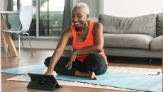 A person using a tablet while sitting on a yoga mat and preparing to exercise