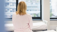 A person sitting on a hospital bed with her back to the camera.