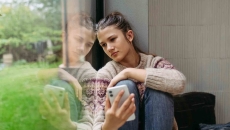 Person sitting by a window while holding a phone