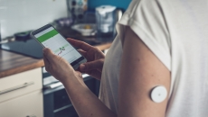 Person wearing CGM patch tracks data on mobile app