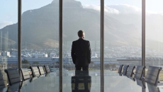 Person standing by a large window with their back turned looking at a large mountain