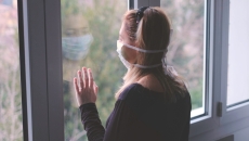 Person with a mask on standing by a window looking out