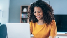 Person sitting at a table while looking at a computer and smiling