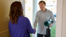 A physical therapist greeting a patient at the door with a yoga mat