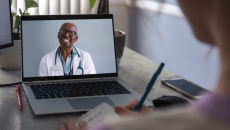 Physician interacting remotely with a person via laptop