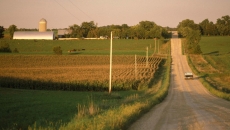 A truck driving on a gravel road near a farm