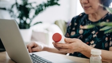Person holding a prescription bottle while using a laptop