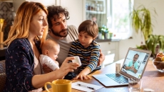 Parents with two young children talk to a provider through a video call on their laptop.