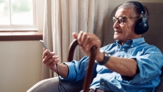 An older man wearing headphones and holding a smartphone