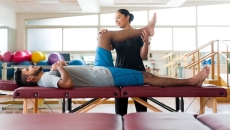 A male patient lying on his back on a massage table and a female physical therapist holding his leg up.