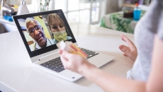 A close up of a woman holding a prescription while talking to two providers on her laptop