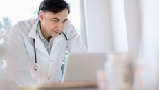 Healthcare provider wearing a lab coat with a stethoscope around their neck while looking at a computer