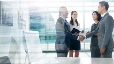 Four people standing in a room with two of them shaking hands