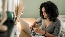 A woman using a laptop with a spreadsheet on her desk.