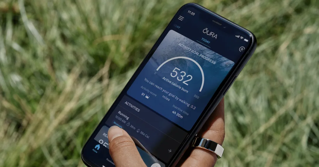 A close-up of a person wearable an Oura Ring with a smartphone running the Oura app