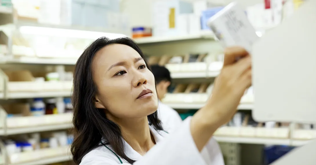 Pharmacist in a pharmacy looking at a piece of paper while holding it up to the light Pharmacist in a pharmacy looking at a piece of paper while holding it up to the light