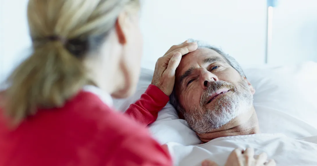 Person in a red shirt sitting next to someone in a hospital gown lying in a bed
Person in a red shirt sitting next to someone in a hospital gown lying in a bed