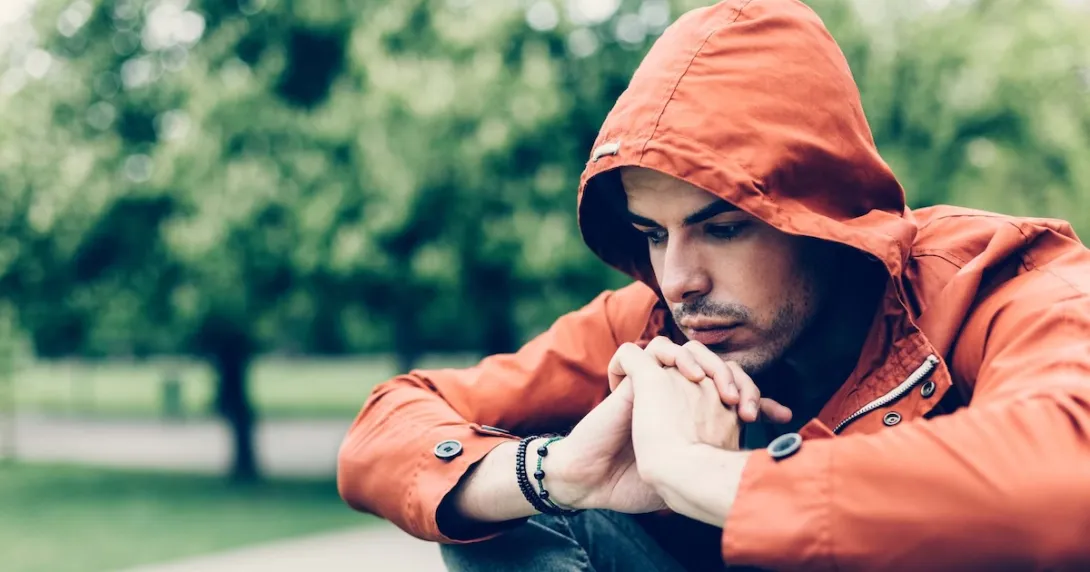 Person sitting in a park while wearing an orange sweater with a hood Person sitting in a park while wearing an orange sweater with a hood