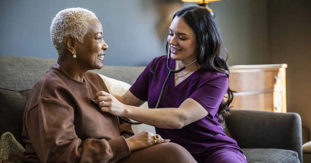 Healthcare provider sitting on a couch with a patient in their home checking their vitals.
Healthcare provider sitting on a couch with a patient in their home checking their vitals.