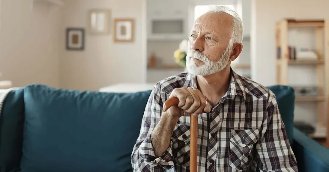 Person sitting on a couch looking away from the camera while holding a wooden cane
Person sitting on a couch looking away from the camera while holding a wooden cane