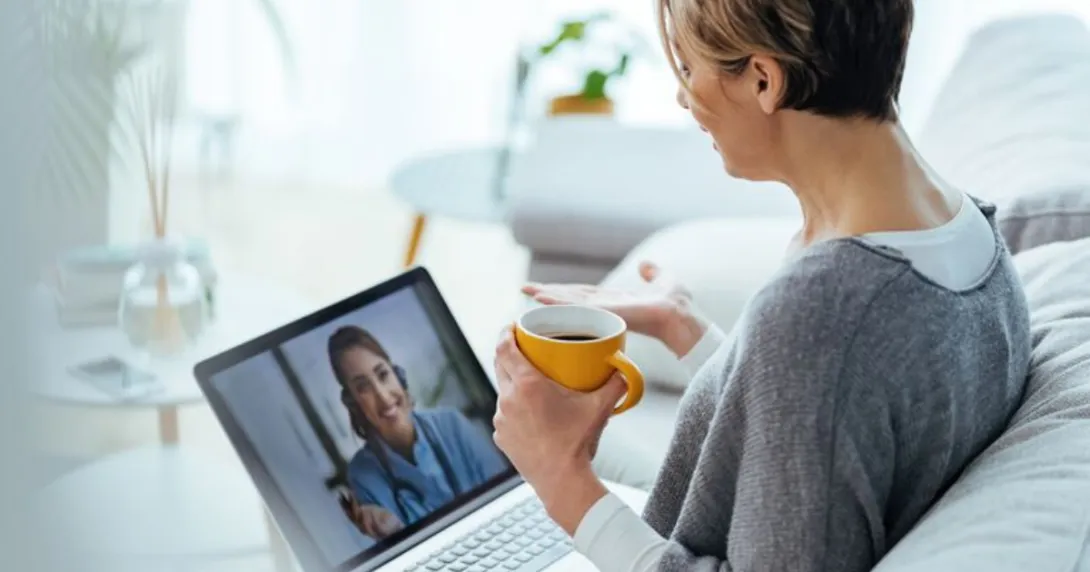 Person sitting on a couch while holding a cup and talking to a healthcare provider on their computer Person sitting on a couch while holding a cup and talking to a healthcare provider on their computer