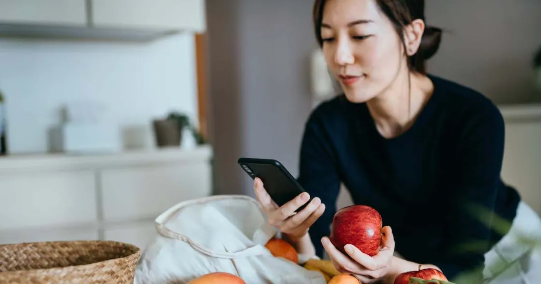 Person leaning against a counter holding an apple while looking at their phone
Person leaning against a counter holding an apple while looking at their phone