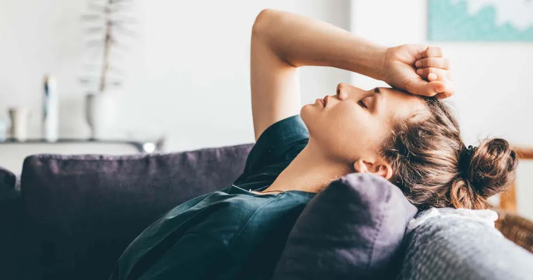 Person lying on a couch with their hand on their forehead with their eyes closed
Person lying on a couch with their hand on their forehead with their eyes closed
