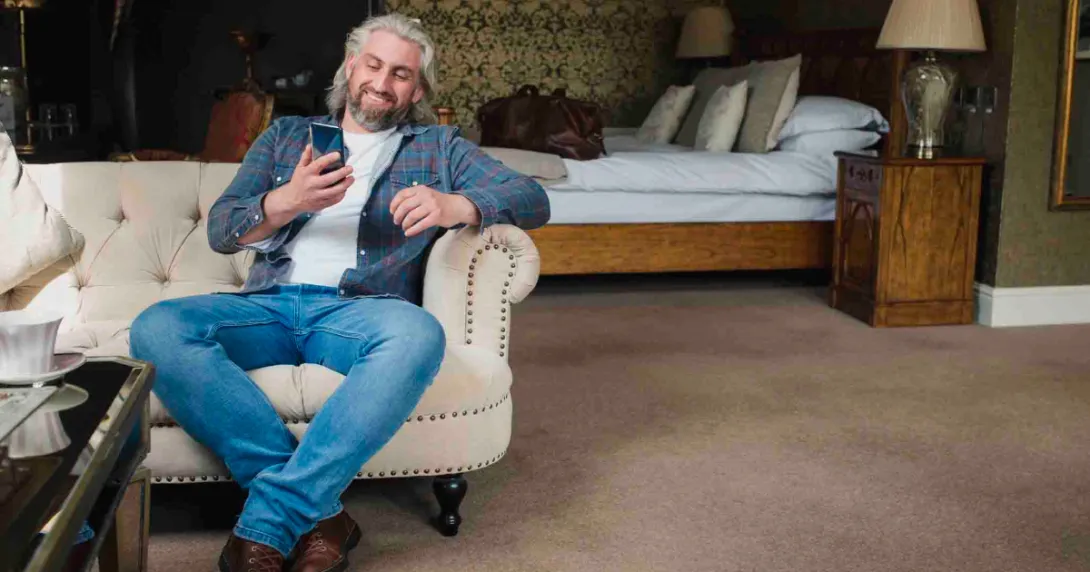 Person sitting on the couch in a hotel room smiling and looking at their phone Person sitting on the couch in a hotel room smiling and looking at their phone