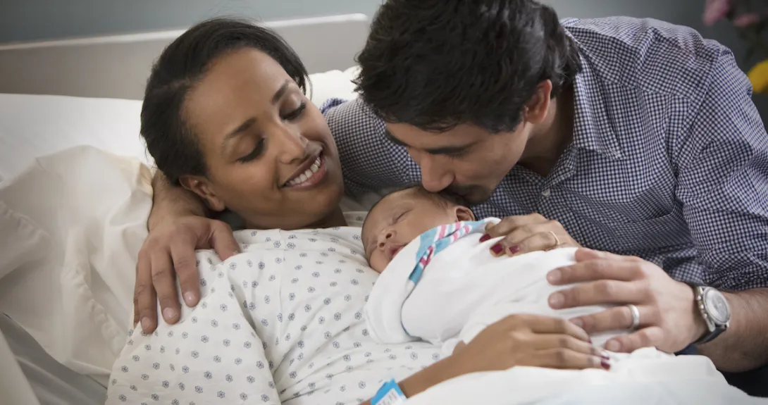 A person laying in a hospital bed with a newborn on their lap and another person standing beside them
A person laying in a hospital bed with a newborn on their lap and another person standing beside them