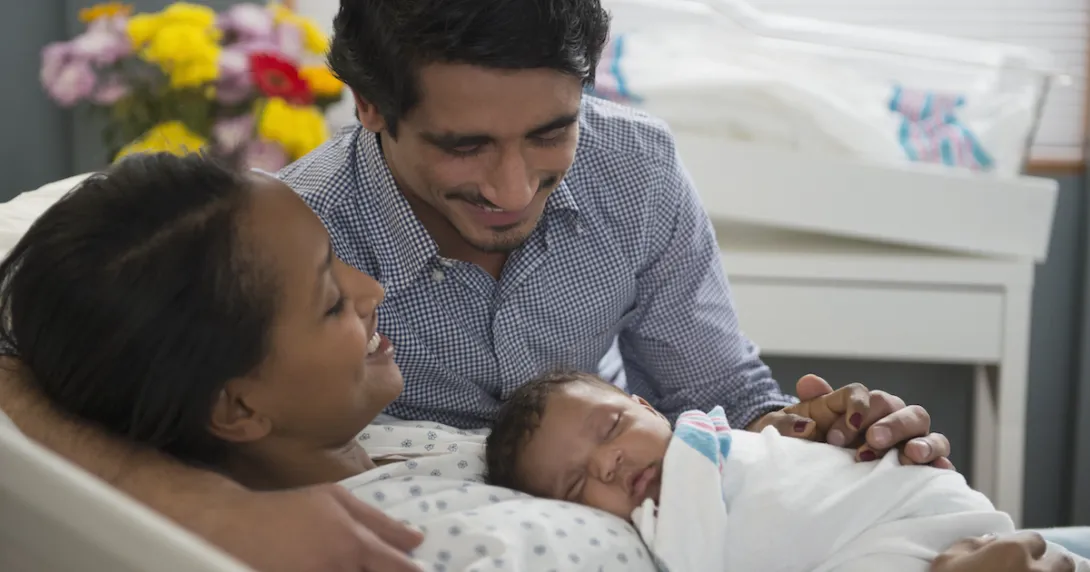 Two people, one lying in a hospital bed and the other leaning over the bed, with both looking at a baby
Two people, one lying in a hospital bed and the other leaning over the bed, with both looking at a baby